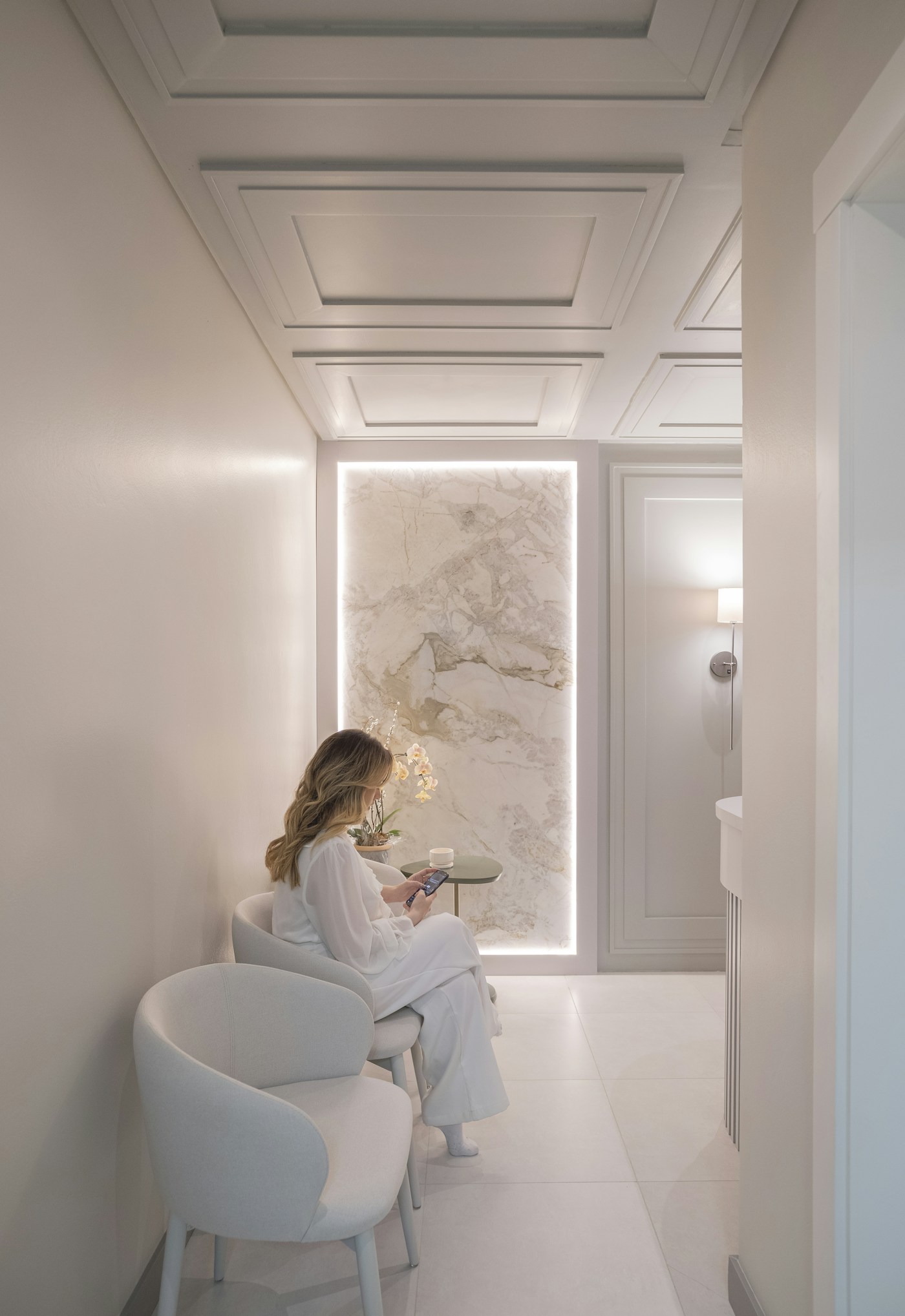 A woman in white seated in an elegant interior with softly illuminated marble
